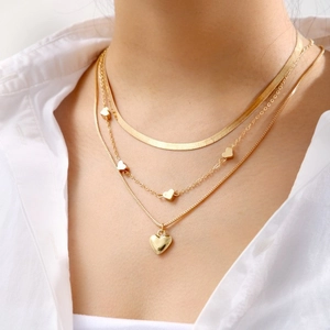 Detailed view of triple-layered gold snake chain necklace with gold heart charms on model