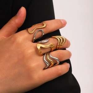 Close-up of stacked gold and silver wave-shaped stainless steel rings on a hand
