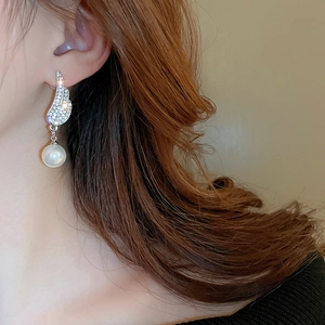 Close-up of silver wing earrings with zircon stones and a hanging pearl drop on a model