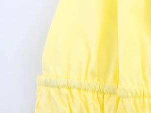Macro view of elasticated smocked hem details on a vibrant yellow halter neck top fabric
