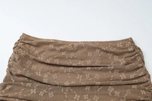 Détail du tissu en dentelle marron avec motifs floraux et texture plissée sur fond blanc