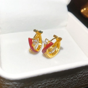Macro detail of gold earrings with red glaze and white zircon stones in a white box