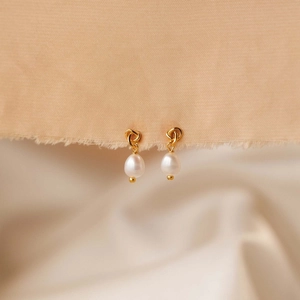 Elegant 18K gold plated knot earrings with white teardrop pearls on soft fabric