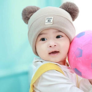 Detail of baby winter knit hat featuring double brown pom-poms and Moonlight patch label
