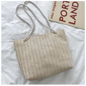 Detailed view of cream straw woven tote bag with rope handles on white textile