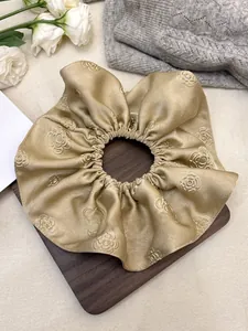Macro detail of champagne gold jacquard satin scrunchie with 3D rose floral embossing