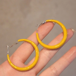 Orecchini a cerchio geometrici gialli minimalisti con perno in argento sulla mano