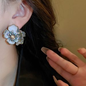 Close-up of vintage flower earrings with white enamel petals and colorful crystals