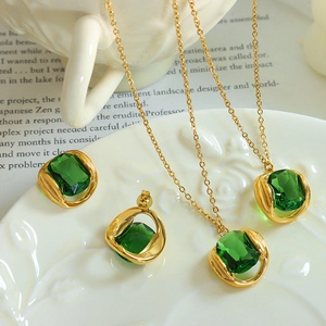 Elegant gold necklace and earring set with emerald green crystals on white ceramic