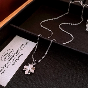 Detail of silver clover pendant on delicate chain inside a brown jewelry box