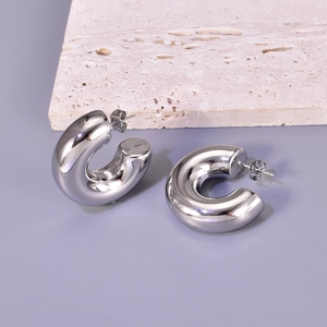 Detailed close-up of hollow silver stainless steel hoop earrings on a textured stone surface