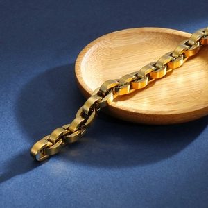Détail macro du bracelet à maillons ovales en or poli sur un plateau en bois minimaliste