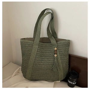 Close-up of green woven straw tote bag featuring decorative wooden bead tassels