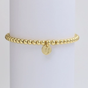 Macro view of golden beaded bracelet featuring a round pendant with engraved letter U