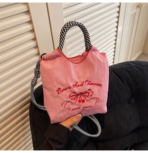Close-up of pink nylon bag featuring cherry embroidery and checkered rope handles