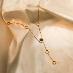 Elegant gold Y-shaped titanium necklace with Roman numeral rings on silk background