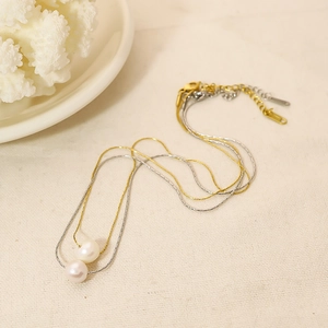 Gros plan sur collier double rangée doré et argenté avec perles blanches sur textile