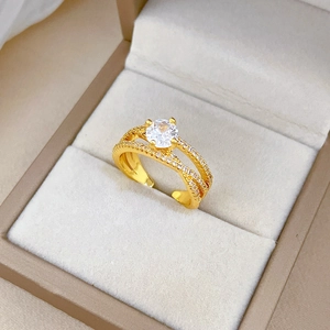 Detailed close-up of golden crossover ring with zircon stones in a beige jewelry box