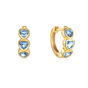 Detail of heart-shaped gold hoop earrings with three vertical blue gemstones on white background