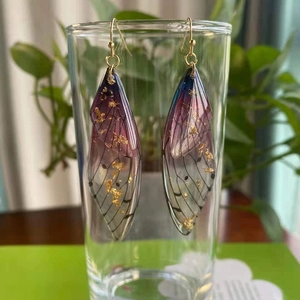 Macro detail of cicada wing earrings with purple gradient and gold foil accents