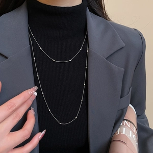 Detail of silver metallic beaded layered necklace worn over a black turtleneck top