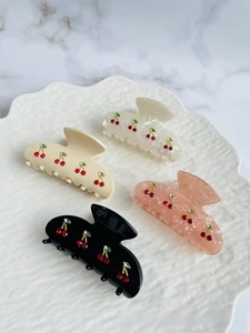 Detailed view of acetate hair claws featuring sparkling rhinestone cherry patterns in various colors