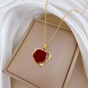 Macro shot of gold heart necklace with red velvet rose and zircon pavé on white silk