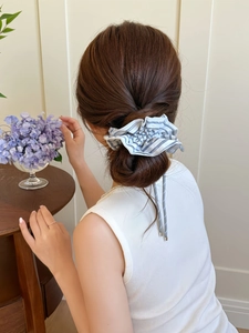 Detail of blue striped scrunchie with ribbons styled on a low bun in a cozy room