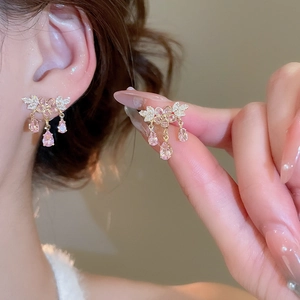 Dettaglio di orecchini a fiore rosa con nappe dorate indossati da una modella