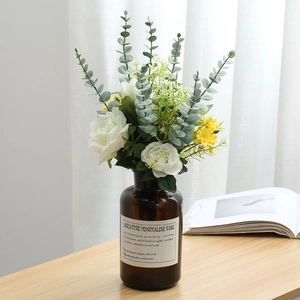 Composizione floreale finta di eucalipto e rose artificiali in un vaso di vetro decorativo.