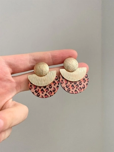 Close-up of geometric wood earrings with leopard print and gold textured metal finish