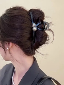 Detail view of a black hair claw clip with pearls and heart rhinestones worn by a model