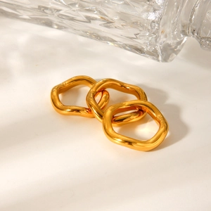 Three gold-plated wavy rings stacked on a white surface with warm natural lighting