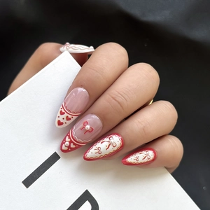 Red heart almond press-on nails with bow designs and 3D pearls on a model hand