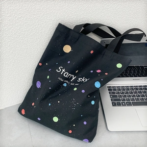 Détail du sac en toile noire avec imprimé planète à côté d'un ordinateur
