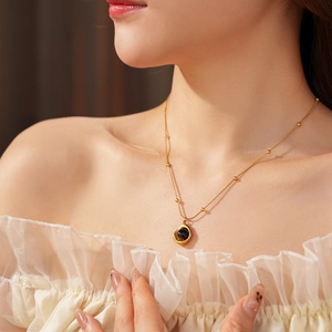 Close-up of golden necklace with black tiger eye stone pendant on model neck