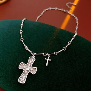 Detail of silver cross necklace with pavé zircons and small plain cross pendant on green velvet