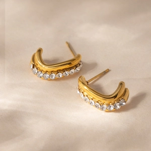 Detail of gold C-shaped earrings with sparkling rhinestones on textured fabric