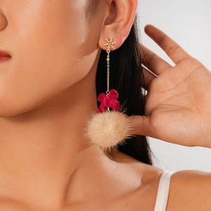 Close-up of model wearing winter snowflake earrings with red bow and beige fur ball detail