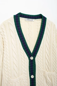Detail of cable knit texture and navy green striped V-neck on beige cardigan