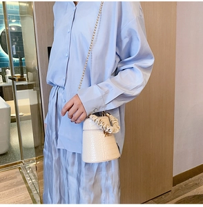 Detail of off-white crocodile embossed bucket bag with golden chain and gathered handle