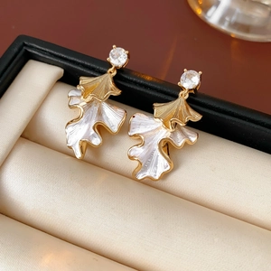 Macro shot of gold-rimmed white leaf earrings with a sparkling zircon in a jewelry box