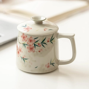 Hand-painted peach blossom ceramic mug with lid in a serene office setting