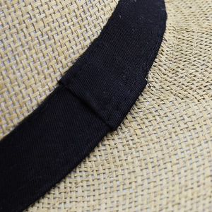 Gros plan sur la texture de paille tressée et le ruban en tissu noir du chapeau de soleil