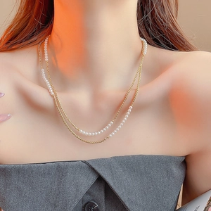 Gros plan d'un collier double épaisseur avec chaîne dorée et perles blanches