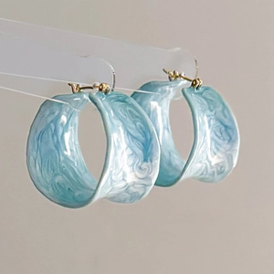 Détail de créoles en émail bleu clair effet marbré avec accents en métal doré poli