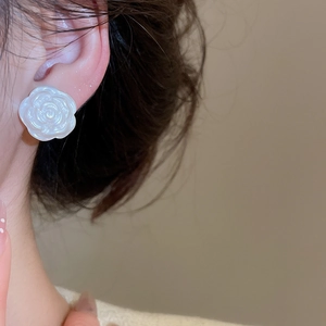 Close-up of white camellia flower earring with pearl-like finish worn on a model ear