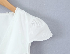 Detail of white V-neck cotton top showing intricate floral embroidery and lace trim