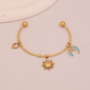 Detailed macro view of gold-tone open bangle with heart, sun, and moon charms