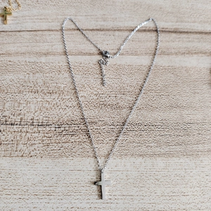 Macro detail of a silver stainless steel cross pendant with an adjustable fine link chain
